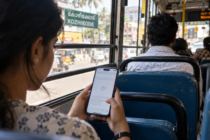 Young person using a smartphone with a loading website on a public bus in Kozhikode, illustrating mobile friendly websites and responsive browsing.